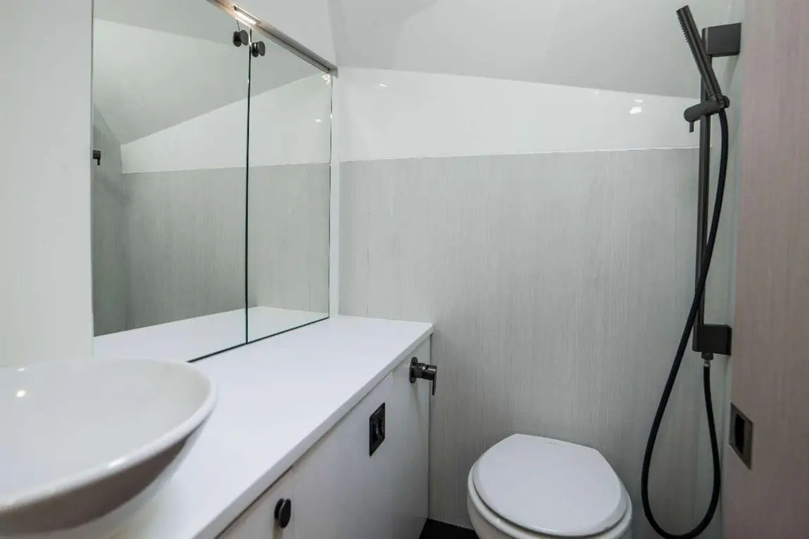 Modern bathroom featuring a white countertop, circular sink, a toilet, and a shower with a hose. Sleek, minimalist design.